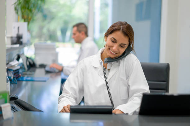 Receptionist working at a doctor's office and talking on the phone Latin American woman working as a receptionist at a doctor's office and talking on the phone -healthcare and medicine services concepts secretary stock pictures, royalty-free photos & images