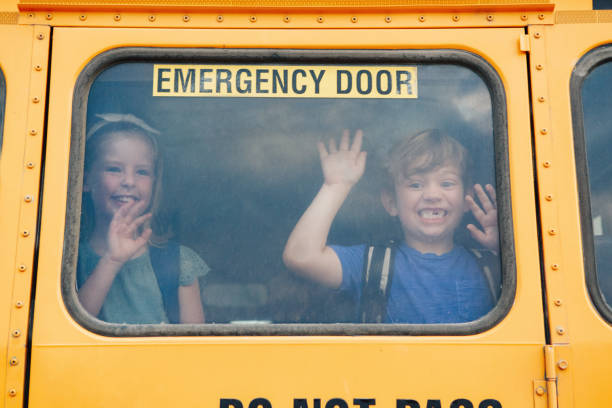 divertidos niños sonrientes y niñas estudiantes que miran por la ventana amarilla del autobús de la escuela. saludando despidiéndose de los padres antes de que comience el día escolar. reunión de compañeros de clase después de las vacaciones de ver - bus door fotografías e imágenes de stock