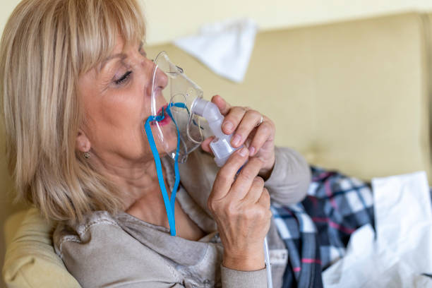 istock An Older Sick Woman is Lying in her Bed Covered with a Blanket and Using Inhaler. 1333461197