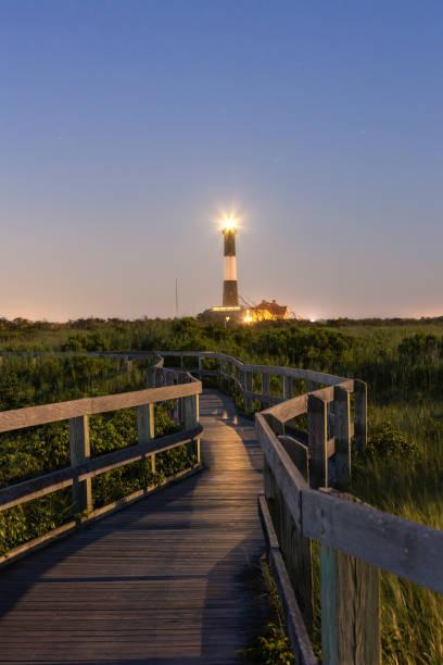istock Wooden boardwalk trail illuminated by a tall lighthouse beacon at night 1333465725