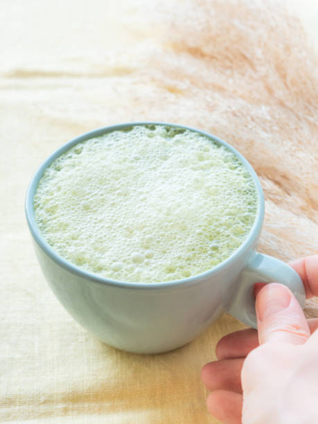 Matcha tea latte morning antioxidant hot drink in blue cup on yellow table cloth with pampas grass