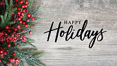 Happy Holidays Text with Holiday Evergreen Branches and Red Berries Over Rustic Wood Background