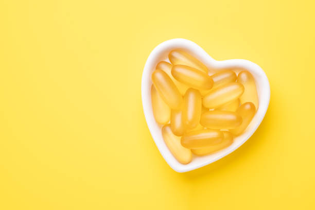 Omega 3 capsules in a heart-shaped plate on yellow background. Fish oil softgels. Copy space. Top view stock photo