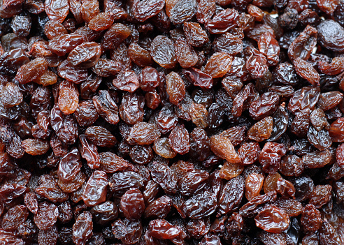 Dark blue raisins in a wooden bowl on a light background. The concept of dried fruits, healthy snacks.