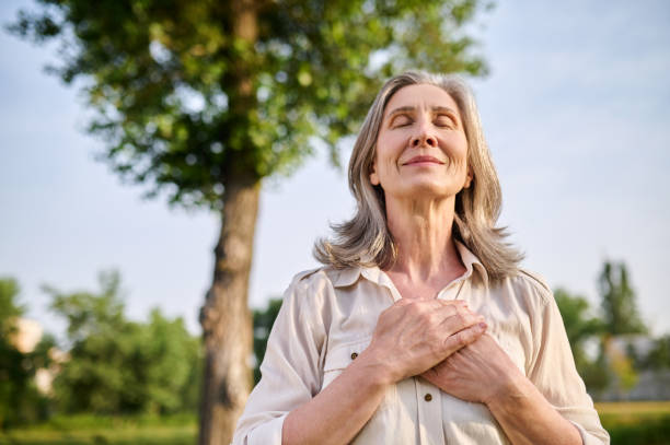 Happy woman folded hands on her chest Calmness. Happy adult smiling woman with closed eyes folded hands on her chest in summer park mental wellbeing stock pictures, royalty-free photos & images