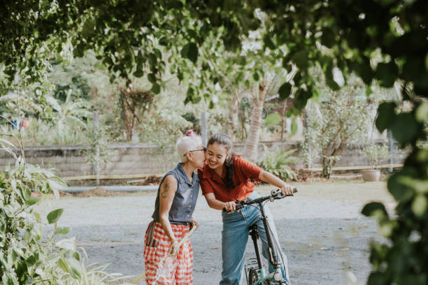emeryt aktywna starsza kobieta całująca córkę podczas podlewania gaju w ogrodzie - zdjęcie stockowe - mental health women asian ethnicity bicycle zdjęcia i obrazy z banku zdjęć