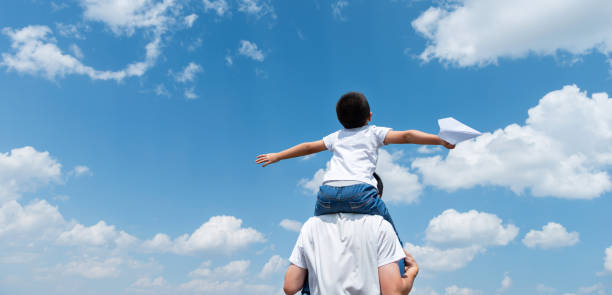 istock Boy sitting on father's shoulder playing paper airplane 1333504613