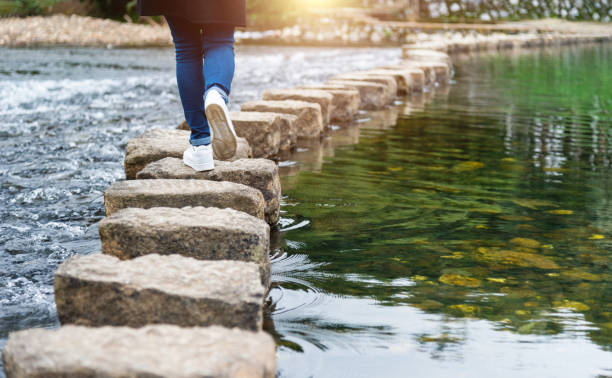 Woman crossing a river on stepping stones stock photo