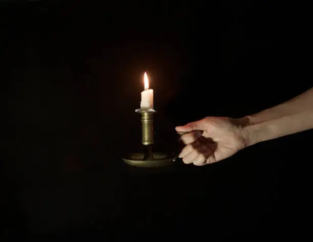 Photo of Decorative copper candlestick with burning candles in a female hand on a black background