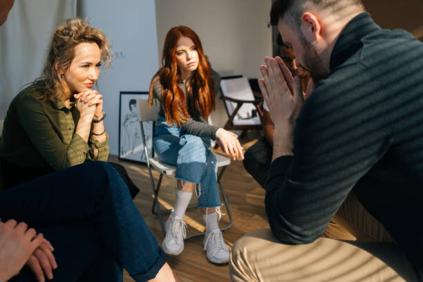 Close-up side view of sad depressed young man talking about problems on group interpersonal therapy session sitting on chairs in circle.