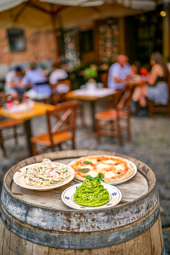 Some famous and delicious dishes of the Italian culinary tradition at the entrance of a typical restaurant in the ancient district of Trastevere, in Rome, with spaghetti in Genoese pesto sauce, Margherita pizza and pasta with carbonara sauce. Image in High Definition format.