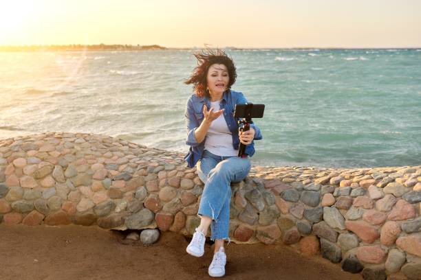 istock Middle-aged female making online video call talking laughing, sunset seascape background 1333509287