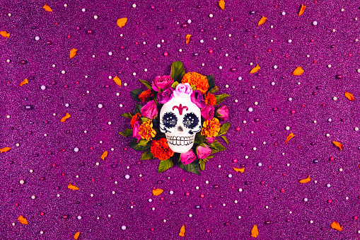 Day of the dead, Dia De Los Muertos. Mexican culture Celebration glitter Purple Background. Sugar Skull, calaverita, marigolds flowers, roses. Traditional festival flyer. Flat lay, top view.