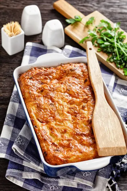 savory potato kugel, baked pudding or casserole of grated potato in a baking dish on a wooden table, jewish holiday recipe, vertical view