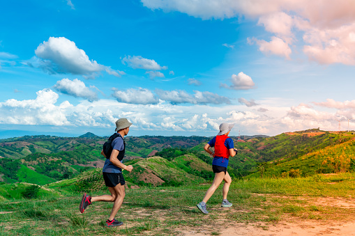 Two Asian men and women trail runners, wearing sportswear, are practicing on a high mountain behind a beautiful view of green mountains.