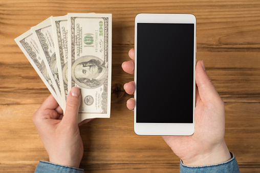 Above photo of smartphone and money cash savings isolated on the wooden backdrop