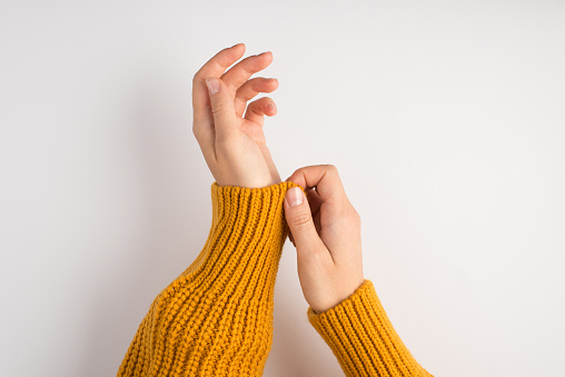 First person photo of woman's hands pulling on sleeve of yellow sweater on isolated white background