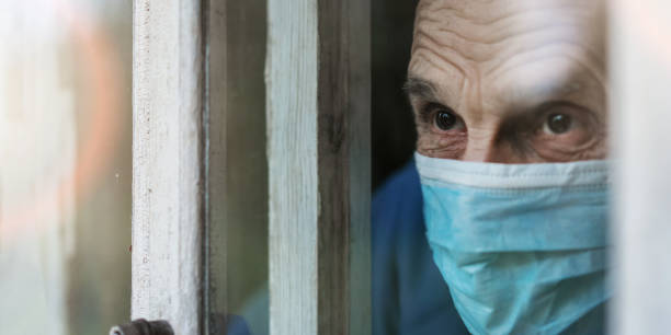 istock Aged person wearing protective face mask stands behind window glass 1333530089