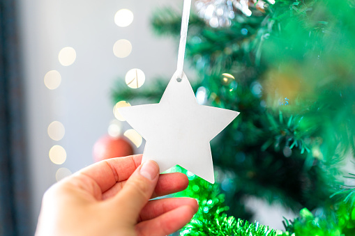 Close-Up Of A Young Woman Placing Star On The Christmas Tree At Home
