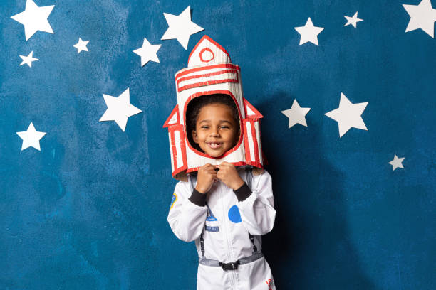 petit garçon afro-américain en combinaison spatiale jouant astronaute sur fond bleu avec des étoiles. enfance, créativité, imagination - imagination photos et images de collection