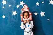 Afro american little boy in space suit playing astronaut on blue backdrop with stars. Childhood, creative, imagination