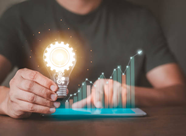 A Man hand holding bright light bulb with graph economic growth success chart on tablet.