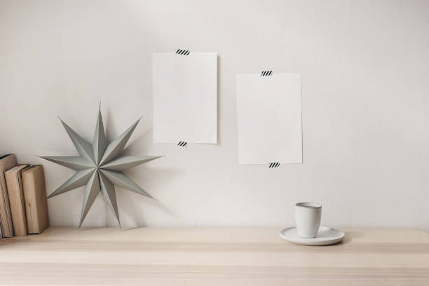 Blank greeting cards taped on white living room wall. Stationery mockup scene with grey folded paper star, cup of coffee and books on wooden table backgroum. Christmas decoration, winter composition. Blank greeting cards taped on white living room wall. Stationery mockup scene with grey folded paper star, cup of coffee and books on wooden table backgroum, Christmas decoration, winter composition. winter still life stock pictures, royalty-free photos & images