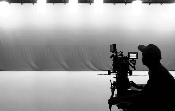 Photo of Video production behind the scenes. Making of TV commercial movie that film crew team lightman and cameraman working together with film director in studio. film production concept. Silhouette style.