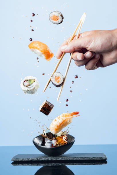 pezzi volanti di sushi su sfondo blu.  formato verticale. - sushi foto e immagini stock