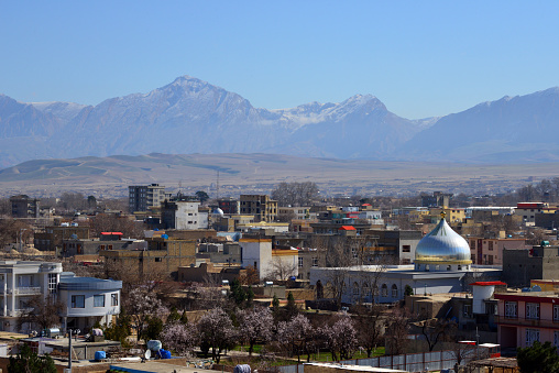 Mazar-e-Sharif, Balkh province, Afghanistan: city skyline - Mosque and city buildings with the mountains in the background. Mazar-e-Sharif is the fourth largest city in Afghanistan, the name of the city means 'Tomb of the Exalted' and refers to the presumed burial place of Ali ibn Abi Talib, cousin and son-in-law of Muhammad, honored by Sunnis, Shiites and Alevis. Mazar is the most important place of pilgrimage in Afghanistan and a holy city of Islam.