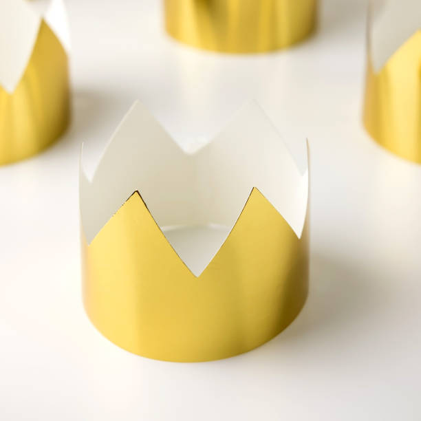 Cardboard golden crowns lying on a white table. Minimalistic style. stock photo