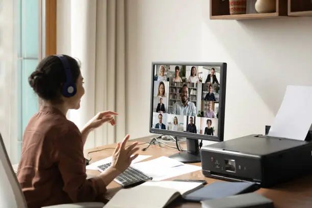 Smiling Indian woman sit at desk at home office talk speak on video call with multiethnic diverse colleagues. Ethnic female employee have webcam digital virtual event on computer with businesspeople.