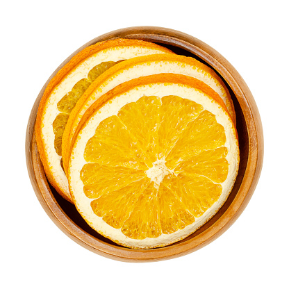 Dried orange slices, in a wooden bowl. Oranges, cut into cross sections, sliced fruits, used as aromatic smelling Christmas decoration. Close-up, from above, isolated on white background, macro photo.