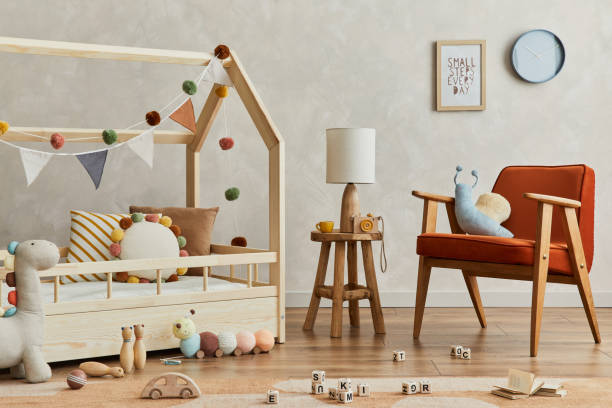 istock Creative composition of cozy scandinavian child's room interior with mock up poster frame, balance board, plush and wooden toys and hanging decorations. Neutral wall, carpet on the floor. Template. 1333551703