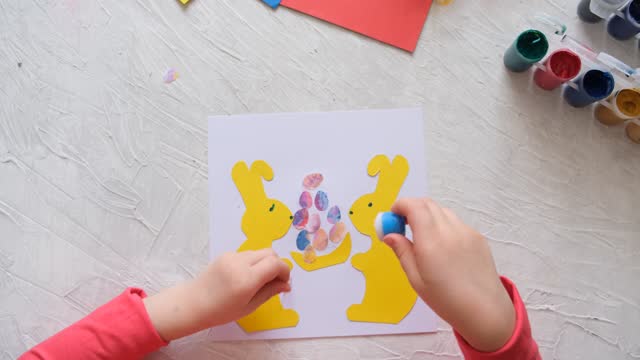Child making card with Easter bunnies  from colorful paper. Applique. Handmade. Project of children's creativity, handicrafts, crafts for kids.