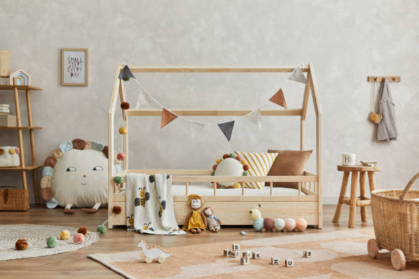 istock Creative composition of cozy scandinavian child's room interior with mock up poster frame, balance board, plush and wooden toys and hanging decorations. Neutral wall, carpet on the floor. Template. 1333551714