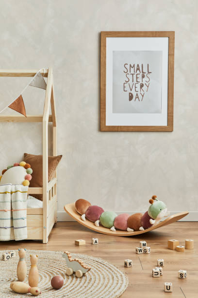 istock Creative composition of cozy scandinavian child's room interior with mock up poster frame, balance board, plush and wooden toys and hanging decorations. Neutral wall, carpet on the floor. Template. 1333551726