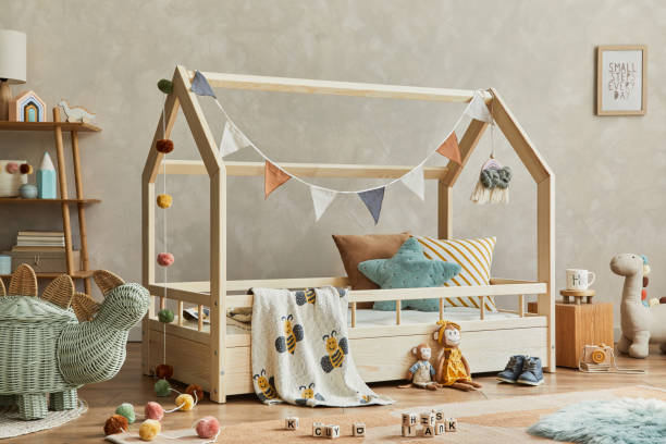 istock Creative composition of cozy scandinavian child's room interior with mock up poster frame, balance board, plush and wooden toys and hanging decorations. Neutral wall, carpet on the floor. Template. 1333551729