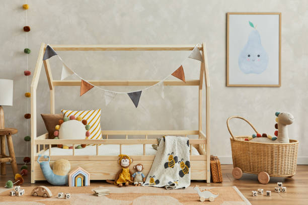 istock Creative composition of cozy scandinavian child's room interior with mock up poster frame, balance board, plush and wooden toys and hanging decorations. Neutral wall, carpet on the floor. Template. 1333551732