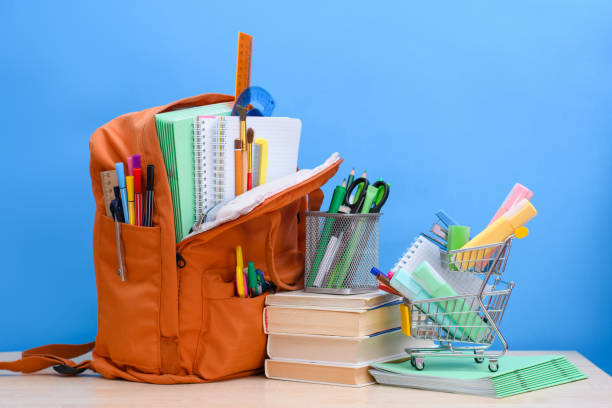 学用品でいっぱいのオレンジ色の学校のバックパックと青い背景に事務用品を持つスーパーマーケットのバスケット。 - school supplies education school equipment ストックフォトと画像