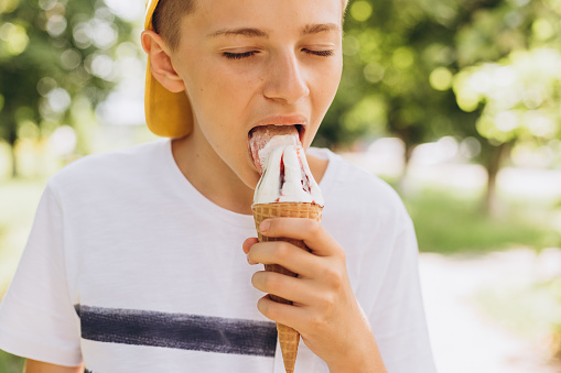 Teenager boy eating ice-cream on nature background. Summer, junk food and people concept