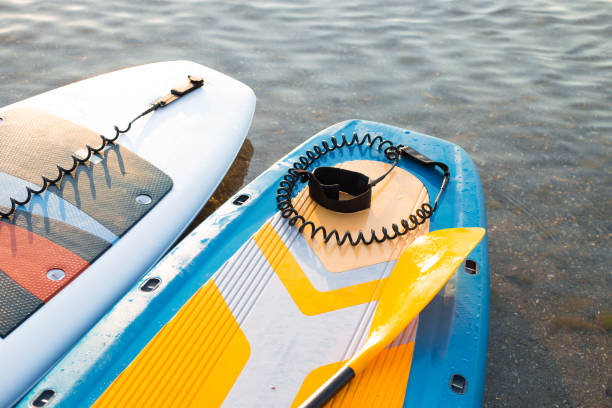 istock Yellow Paddle board and two surf boards on blue clean water surface background. Surfing and SUP boarding equipment in sunset lights close-up. Outdoor water sports. Surfing lifestyle concept. 1333553377