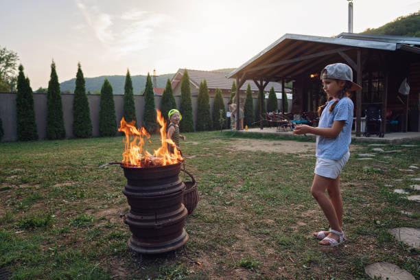Playful and curious siblings, playing around the barbecue flame, throwing the branches into flame, while spending the family da at the country side