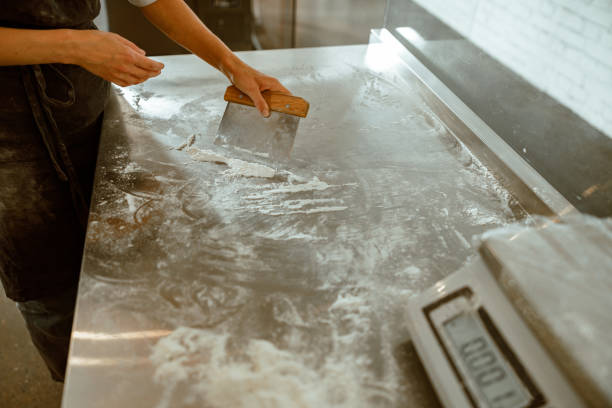 istock Woman worker cleans metal table from flour in modern craft bakery workshop 1333564478