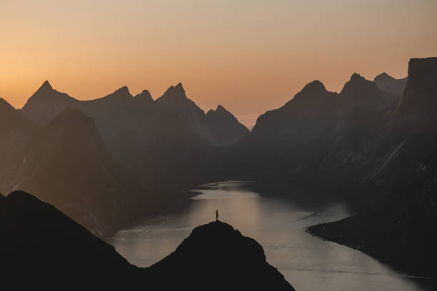 Amazing view of woman in the distant overlooking amazing sunset. View of silhouetted person standing in front of amazing mountain range in Lofoten under the sunset. lofoten photos stock pictures, royalty-free photos & images
