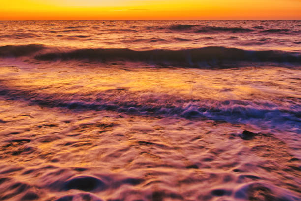 After the sun has set in the ocean, its afterglow prepares a colored evening sky for the viewer on a beach in normandy, france.\nLong exposure used for blurry waves in the foreground.