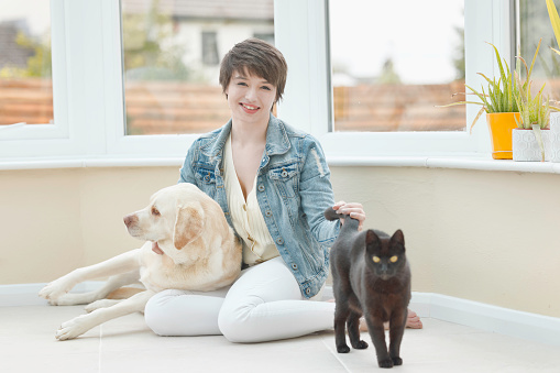 Lady in her twenties with her Yellow Labrador Retriever and black cat in the conservatory. Focus on lady.