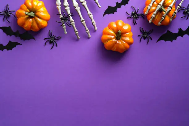 Photo of Halloween flat lay composition with pumpkins, bony hands, spiders, bats on purple background. Happy halloween banner mockup.