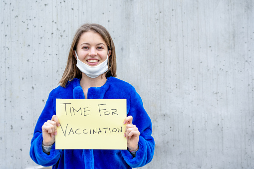 Young woman with a sign inviting to do vaccinations, worldwide medical campaign to defeat the spread of Covid19