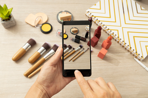 Woman holding smartphone and taking picture,video about beauty products.Online shopping.Makeup tools for sale